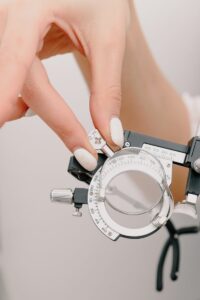 Ophtalmologue féminine méconnaissable avec des mains manucurées démontrant une monture d'essai avec lentille tout en travaillant dans un studio d'optométrie moderne